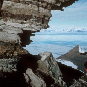 A man standing in front of a large rock next to water.