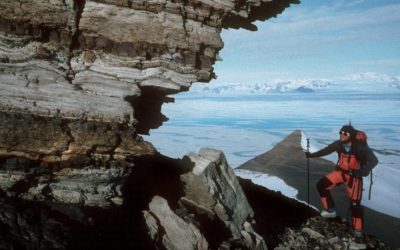 A man standing in front of a large rock next to water.