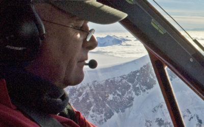 A pilot in the cockpit of an aeroplane flying above mountains