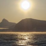 A sunset over a body of water with a mountain in the background.