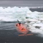An orange submersible is partly visible in the water, with ice floating next to it