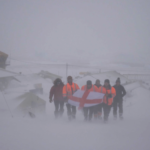 A group of people walking across snow covered ground, holding a flag