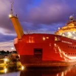 A large red ship in water. It is dark and the ship is lit up.